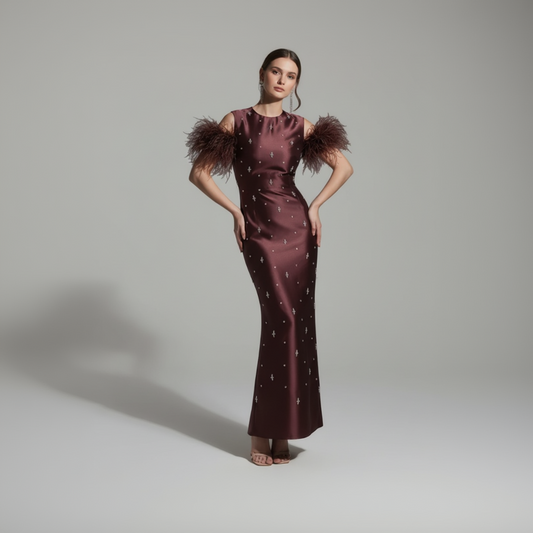 Woman wearing a burgundy evening gown with feathered shoulders against a gray background