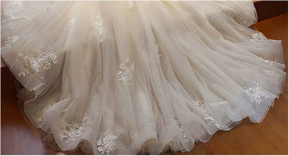 Close-up of a white wedding dress with floral lace details on a wooden floor.
