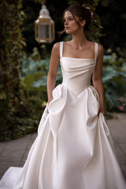Woman in a white wedding dress standing outdoors with greenery in the background
