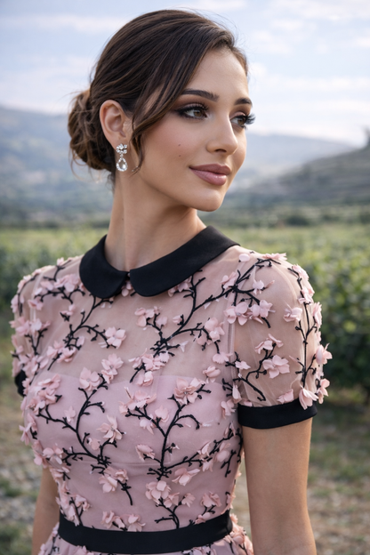 Woman wearing a pink dress with black floral embroidery in an outdoor setting
