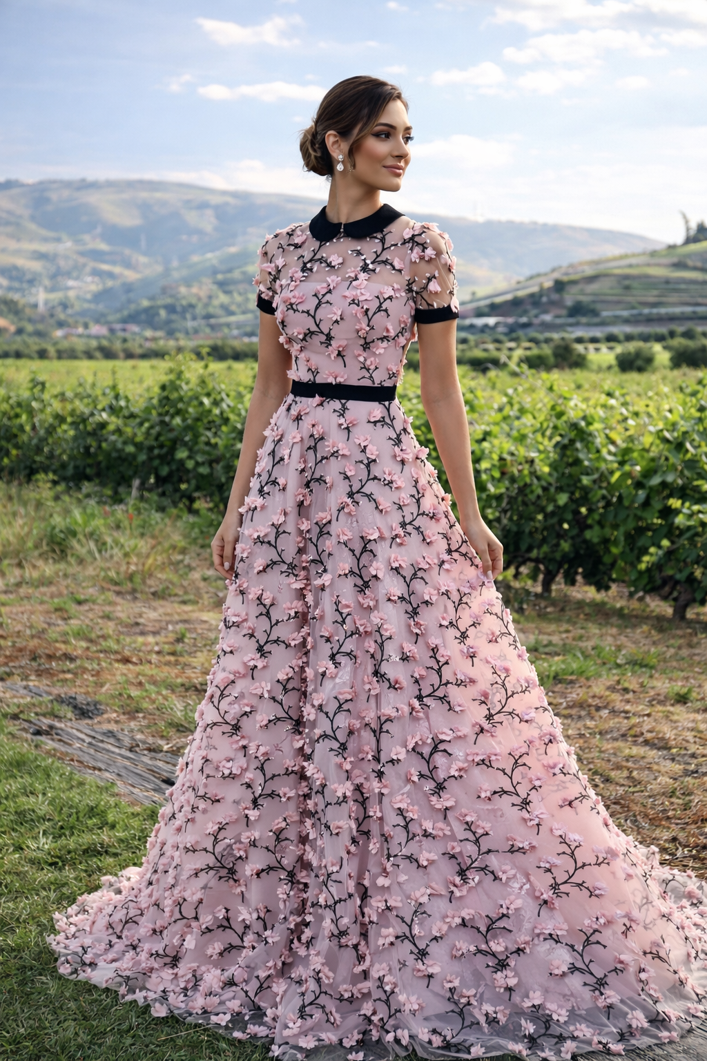 Woman in a pink floral dress standing in a scenic outdoor setting with mountains and greenery.