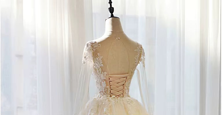 Mannequin wearing a beige evening gown with lace details against a soft white curtain background