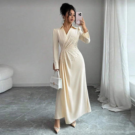 Woman in a long, light-colored dress taking a mirror selfie in a room with gray flooring and white curtains.